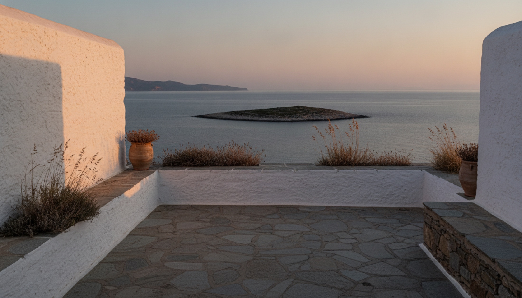 Amorgos'ta Cycladic mimarili bir teras ve karşısındaki ıssız Nikouria adacığı, gün batımı ışığında