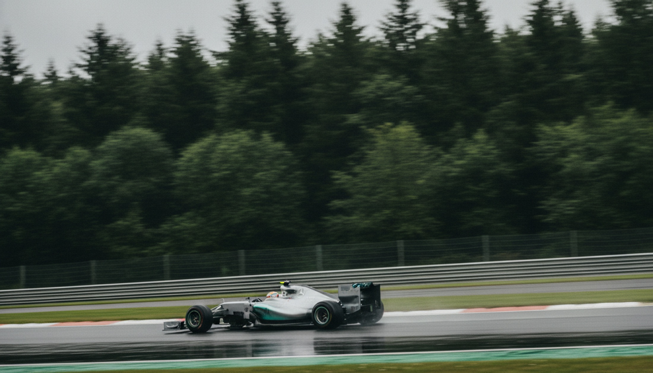 Gümüş Formula 1 aracı, ormanla çevrili hızlı virajda düşük açıdan fotoğraflanmış