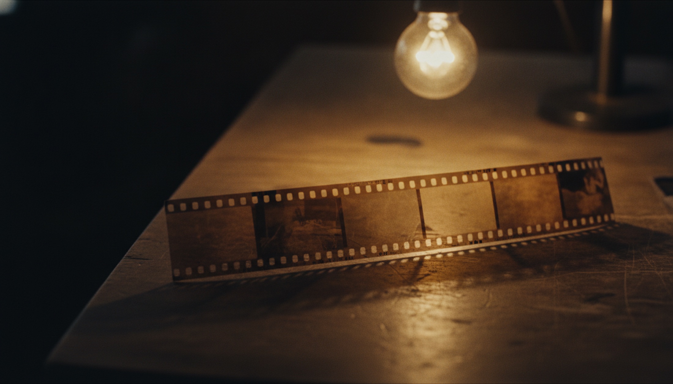 Ahşap kurgu masasında tungsten ışık altında duran 35mm film şeridi, çerçeveler ve perforasyonlar netleşmiş, derin gölgeler
