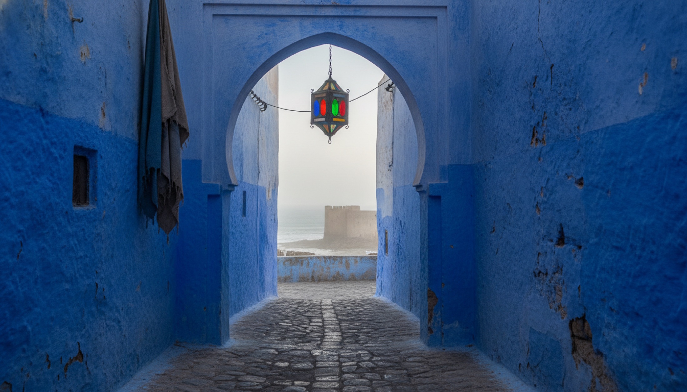 Essaouira medina sokaklarında sabah ışığında mavi-beyaz duvarlar ve asılı fener