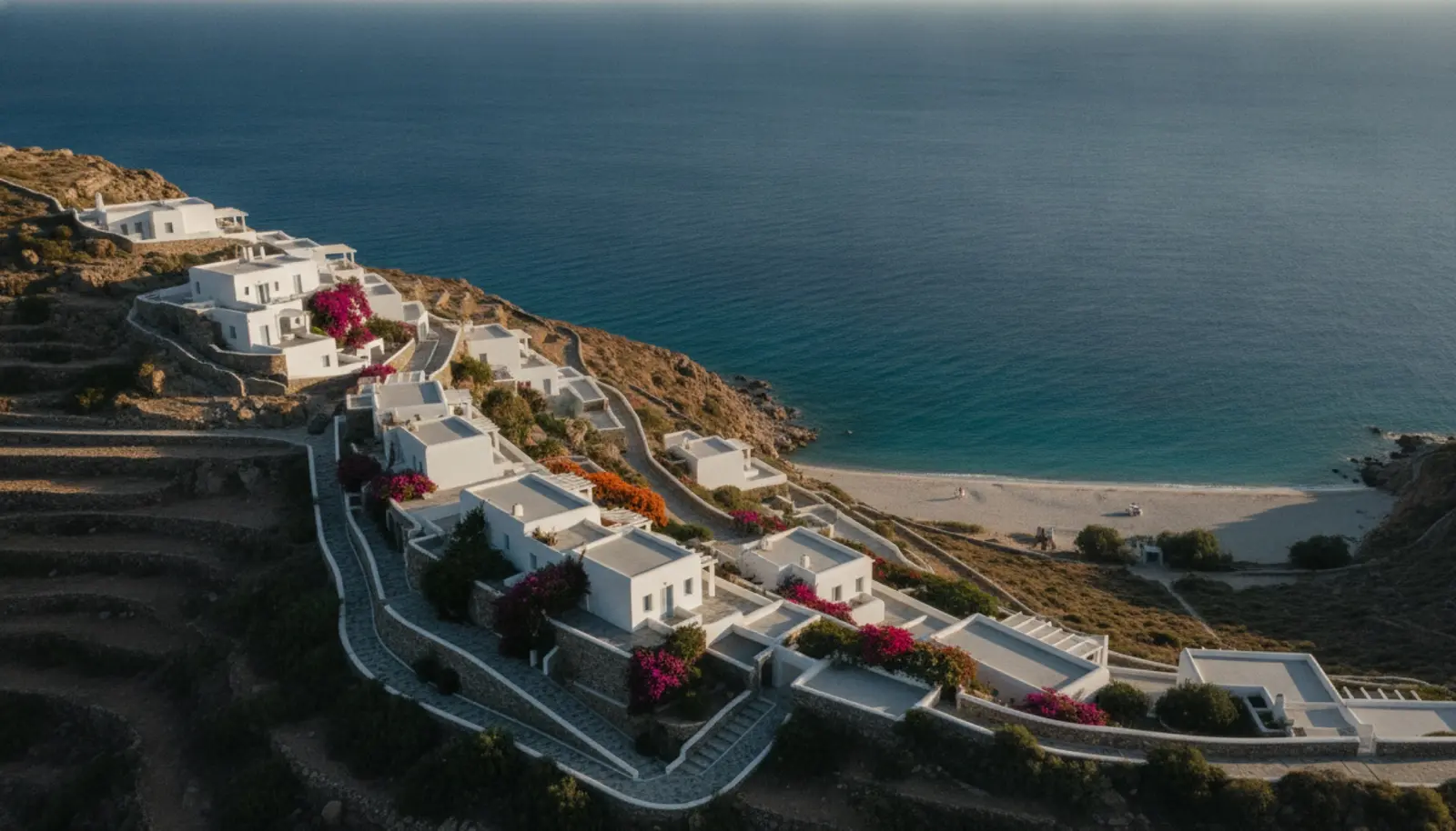 Kalo Livadi Koyu'nun üzerindeki kayalığa yerleşmiş Cycladic mimarili otel, geç öğleden sonra Ege ışığında
