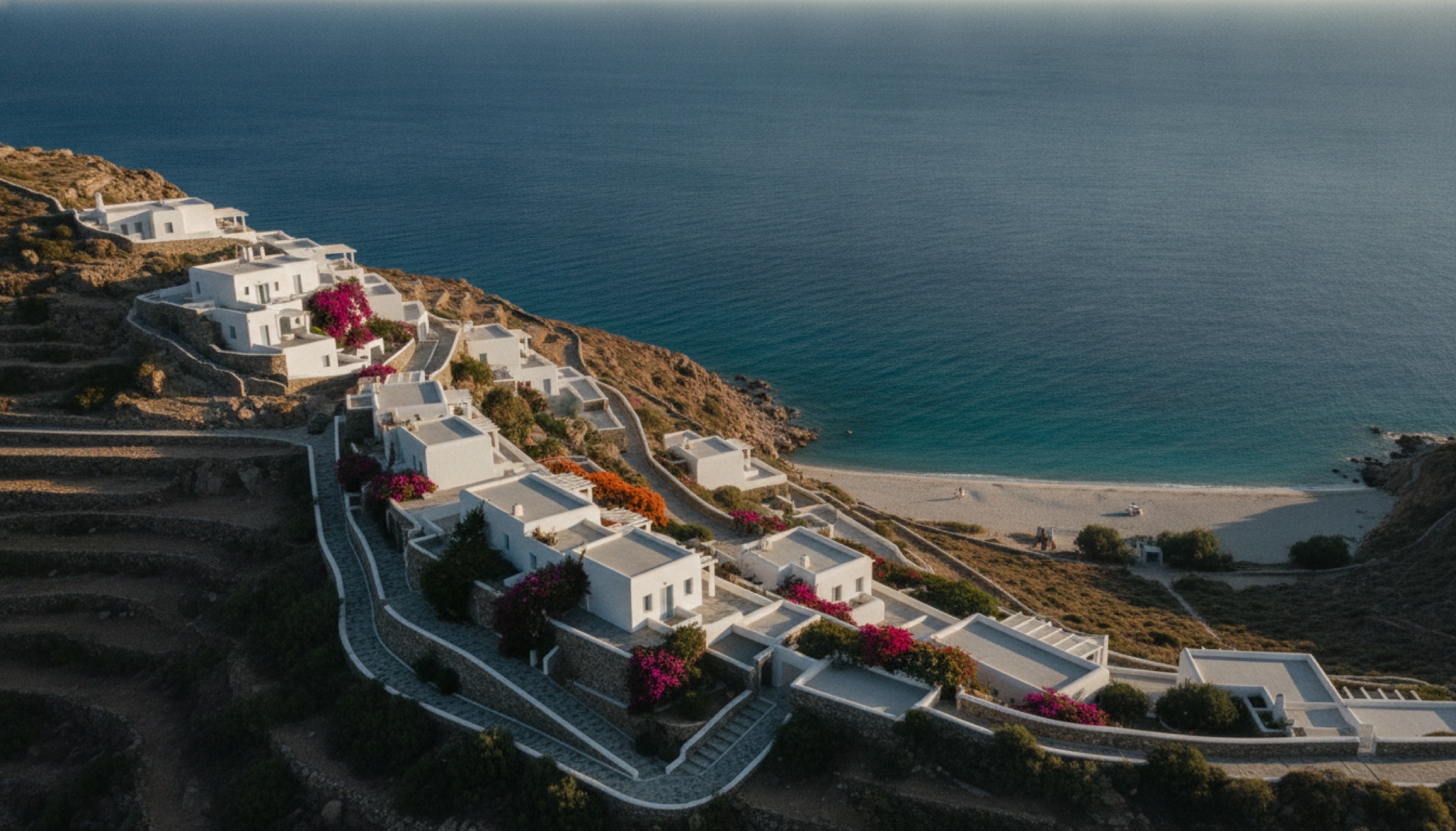 Kalo Livadi Koyu'nun üzerindeki kayalığa yerleşmiş Cycladic mimarili otel, geç öğleden sonra Ege ışığında