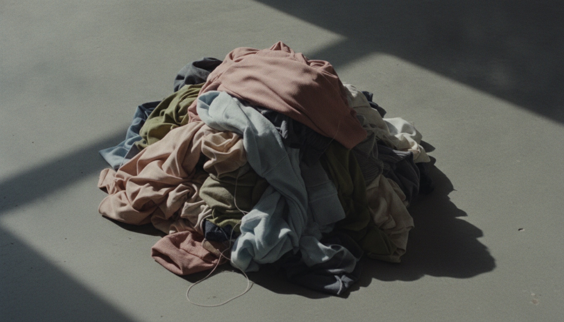 Beton zeminde yığılı sentetik fast fashion kıyafetleri, yukarıdan çekilmiş belgesel fotoğraf