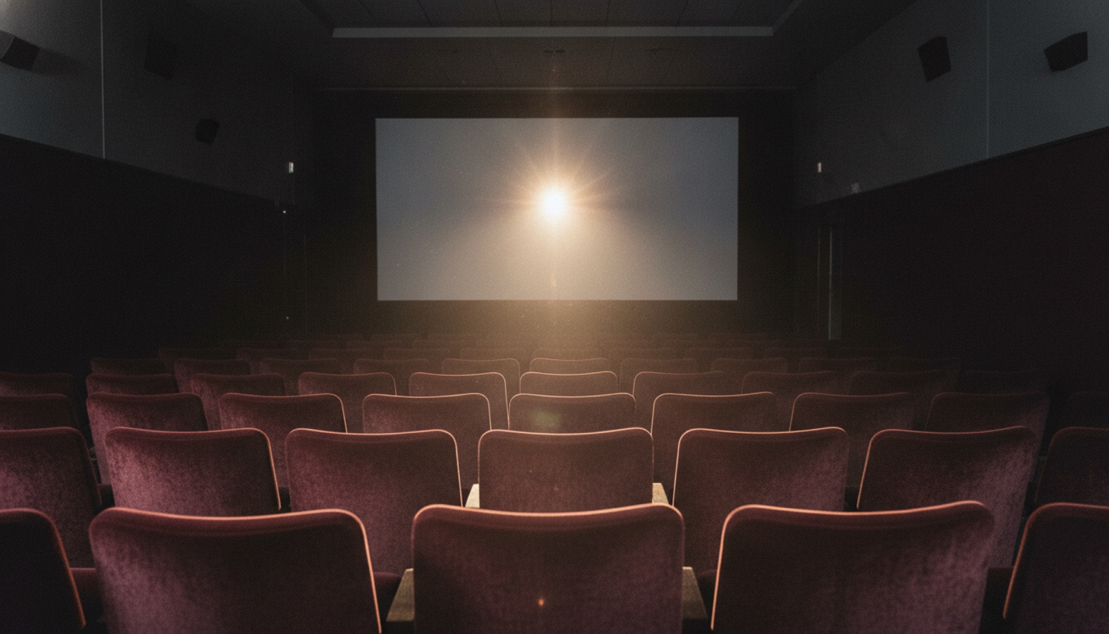 Küçük bir art-house sinema salonunun içi, projeksiyon ışığı boş koltukları ve beyaz perdeyi aydınlatıyor