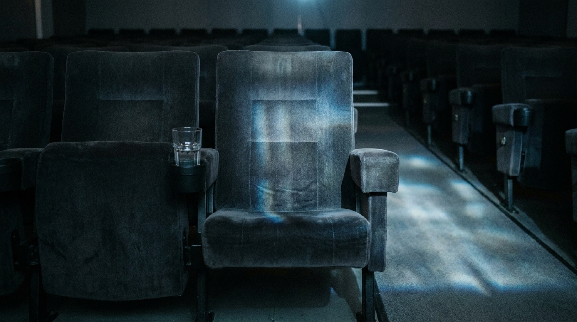 Boş sinema salonunda tek koltuk, kol dayama yerinde bir bardak su, perde yansıması