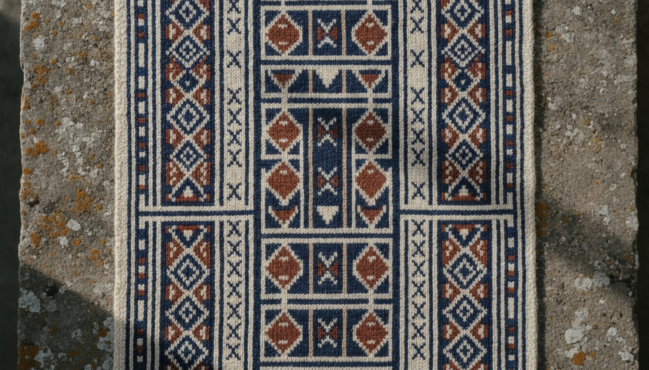 Xhosa boncuk geometrisinden ilham alan zengin desenli örme kumaş detayı, ham taş yüzey üzerinde