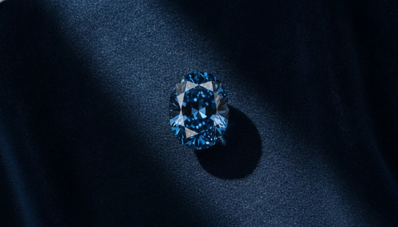 Oval kesimli Fancy Deep Blue mavi elmas koyu zemin üzerinde dramatik ışıkla, derin mavi renk yoğunluğu ön planda
