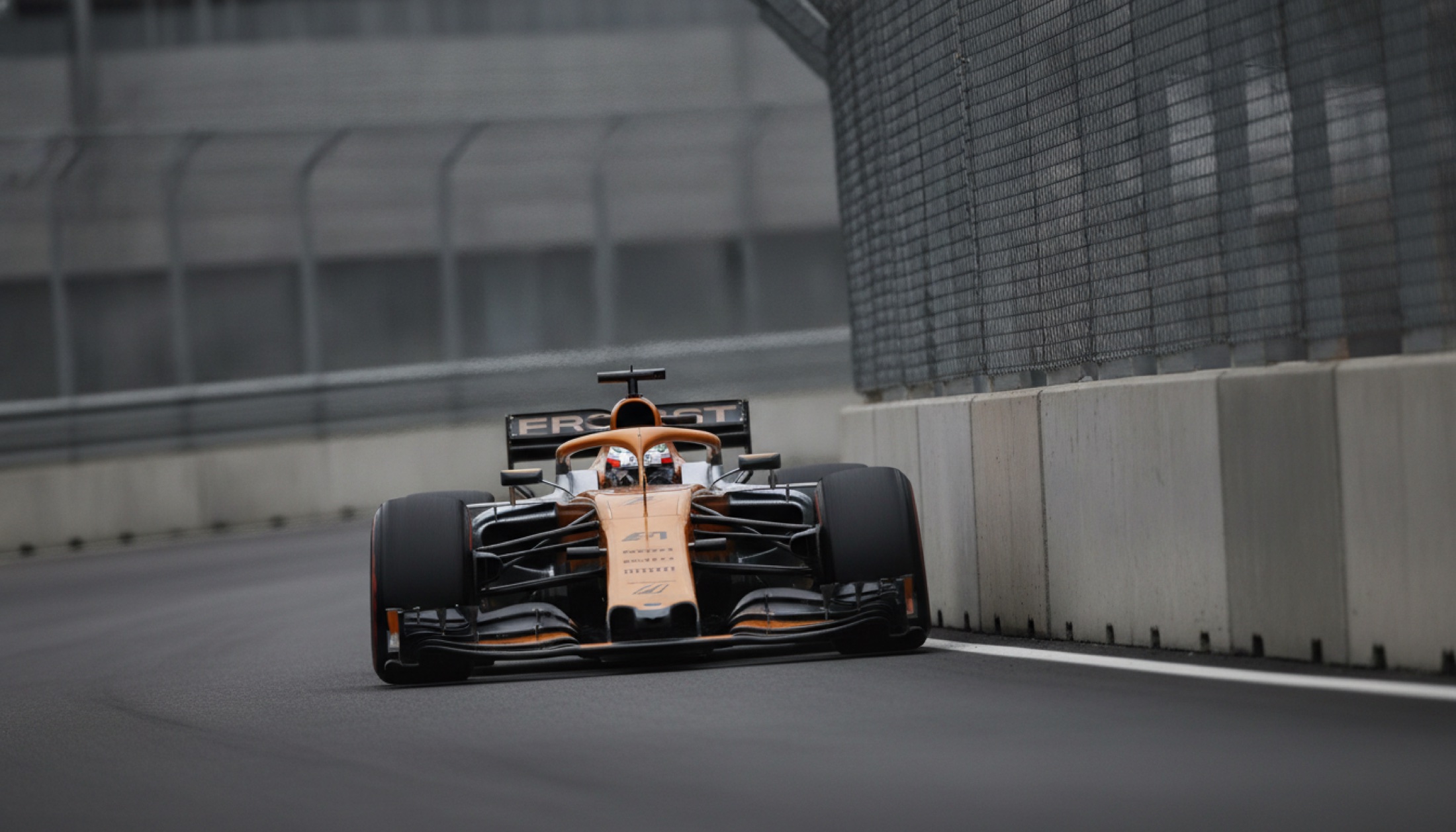 Bir Formula 1 aracı dar virajda, bariyer duvarları yakında, öğleden sonra gri ışıkta
