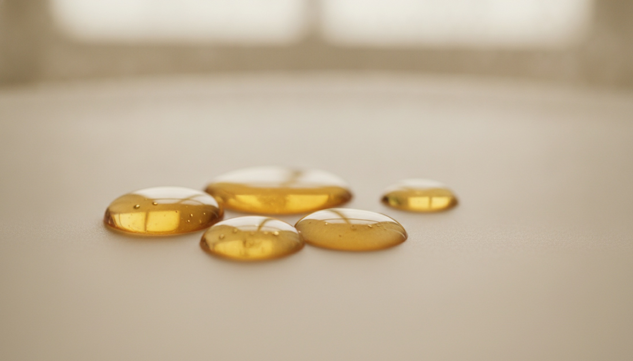 Mat seramik yüzey üzerinde amber rengi serum damlaları, yumuşak doğal ışık altında