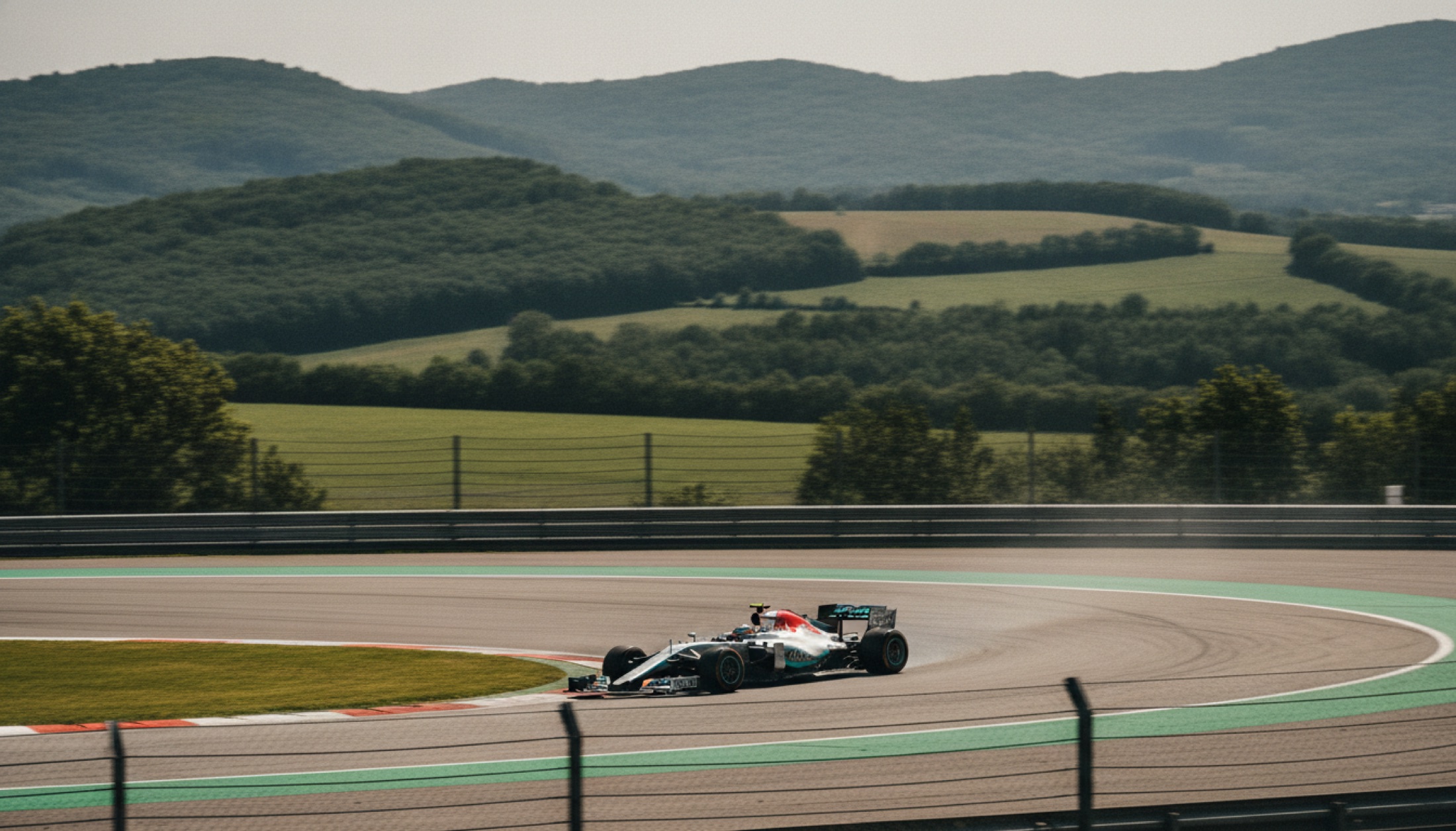 Spielberg'deki Red Bull Ring'de dar bir köşeyi hızla geçen gümüş-turkuaz Formula 1 aracı, yeşil Avusturya dağları arka planda