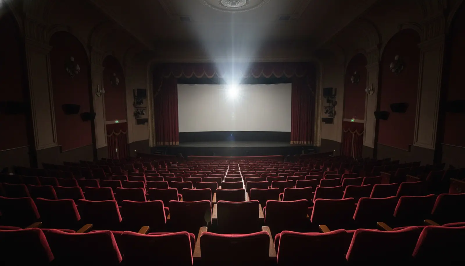Boş bir sinema salonunda koltuk sıralarına uzanan projeksiyon ışığı
